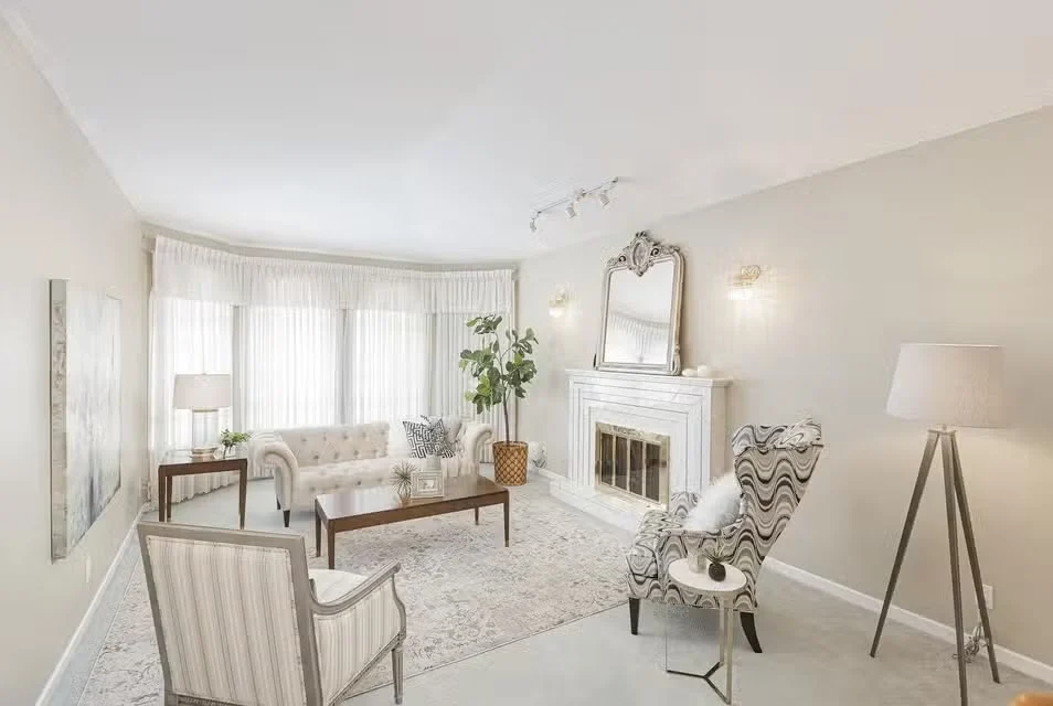 The same living room staged with a tufted sofa, patterned armchairs and layered lighting