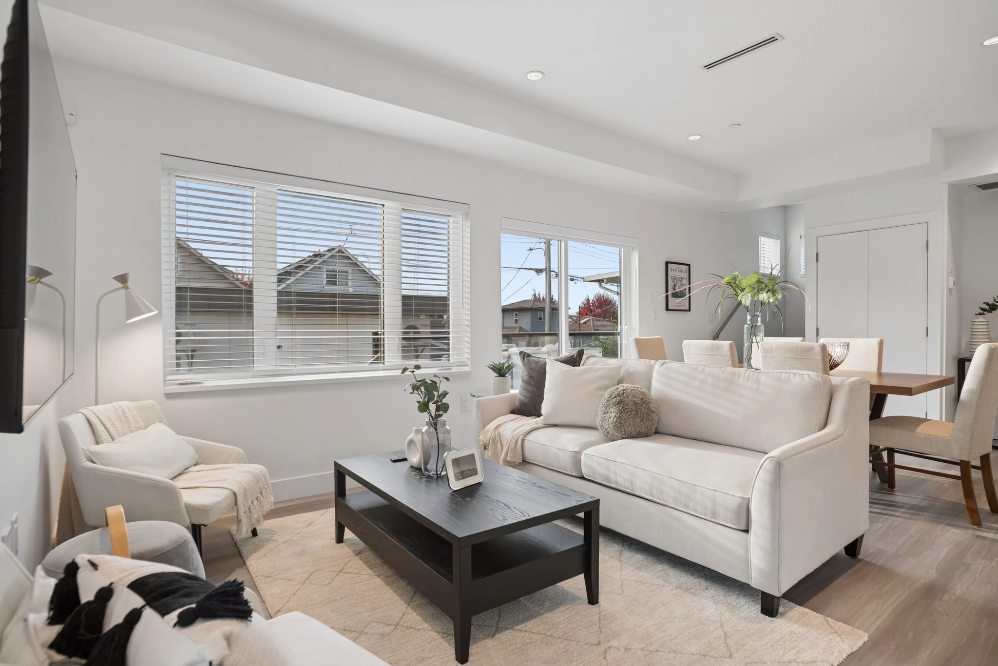 Furnished rental living room: a cream sofa and armchair around a dark coffee table, with the dining table beyond